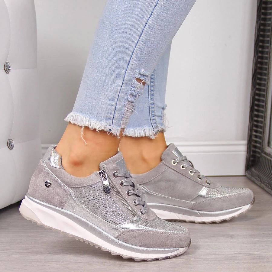 Sneakers gris clair élégants avec lacets classiques, détails métallisés et semelle blanche épaisse, alliant confort orthopédique et style moderne pour un usage quotidien.