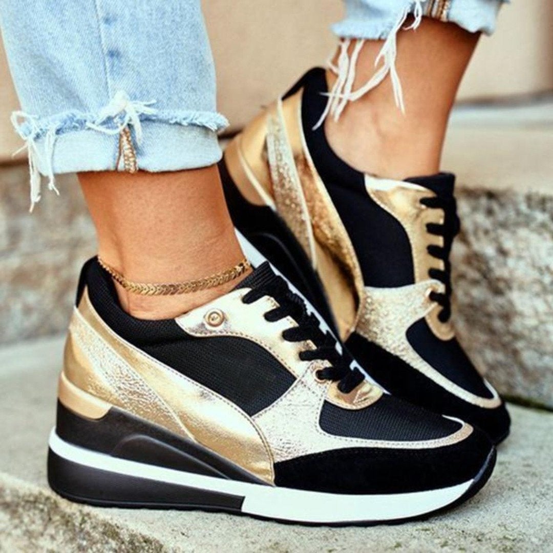 Plan rapproché de baskets noires et dorées élégantes avec une semelle à talon ergonomique et épurée, offrant à la fois élégance et confort. Portées avec un jean retroussé et effiloché et un bracelet de cheville chic, ces chaussures sont parfaites pour un look quotidien à la fois tendance et confortable.