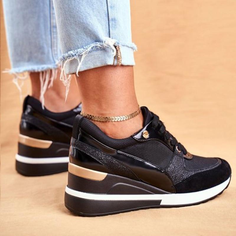 Plan rapproché de baskets noires élégantes avec un talon compensé, présentant un design épuré avec des accents dorés. Les baskets sont associées à un jean bleu déchiré, mettant en valeur un look tendance et confortable, idéal pour une tenue décontractée.