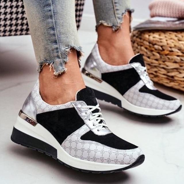Une paire de baskets noires et argentées élégantes au design moderne et épuré, combinant du daim et du tissu imprimé. Les baskets sont associées à un jean bleu déchiré, mettant en valeur le confort et la mode avec une semelle ergonomique pour un soutien supplémentaire.