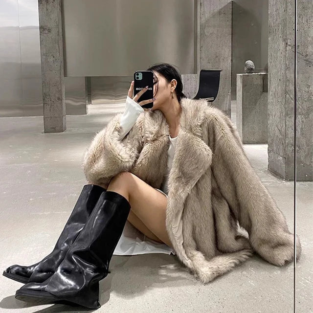 Manteau en fausse fourrure gris-beige porté avec style par une femme assise, combiné à des bottes hautes noires, pour un look hivernal élégant et tendance.