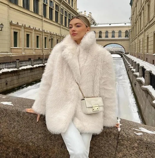Élégant manteau en fausse fourrure blanche porté par une femme en extérieur enneigé, offrant chaleur et style raffiné pour la saison hivernale.