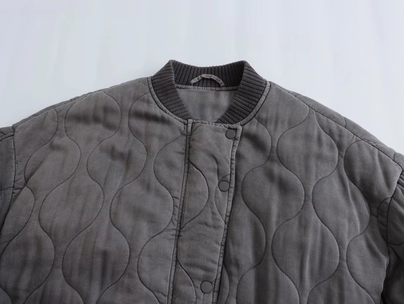 Détail du col et des boutons du blouson long gris "Nancy" pour femme, avec un design matelassé et un bord-côte au niveau du col pour un style moderne et confortable.