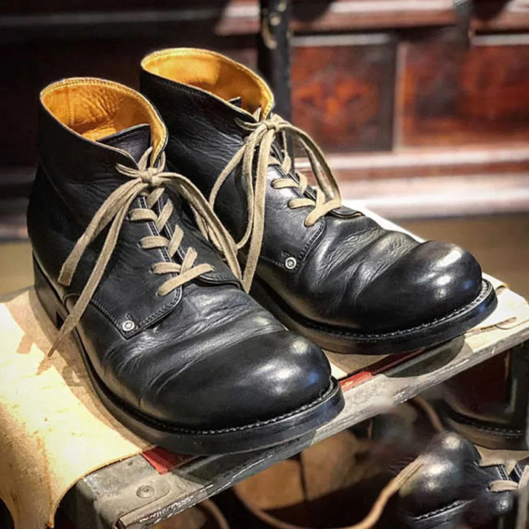Une paire de bottes hautes classiques en cuir noir pour homme, avec des lacets beiges et un intérieur distinctif de couleur moutarde. Ces bottes allient style et durabilité, parfaites pour un port quotidien et suffisamment polyvalentes pour des tenues à la fois décontractées et formelles.