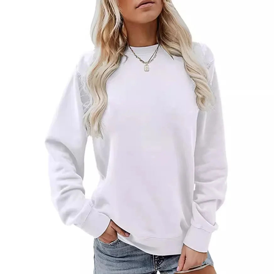 Femme portant un sweat-shirt blanc à manches longues avec un col rond. Elle a une coiffure blonde, porte un collier fin et un short en jean, et affiche une pose décontractée.