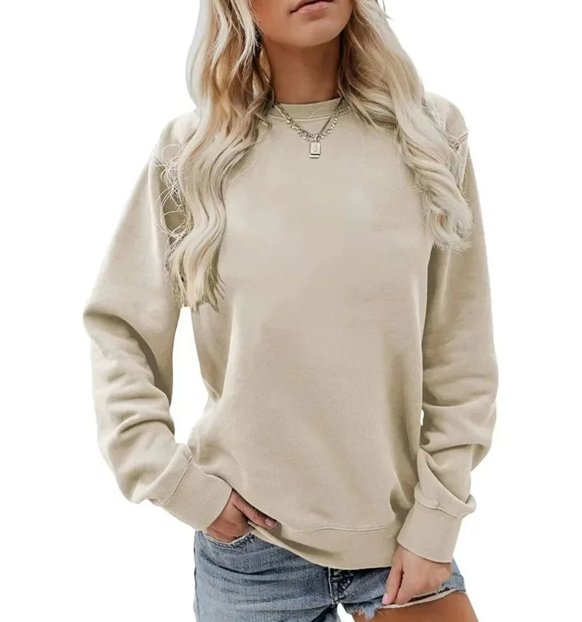 Femme portant un sweat-shirt beige à manches longues avec un col rond, accompagné d'un short en jean. Elle porte un collier délicat et affiche une pose décontractée.