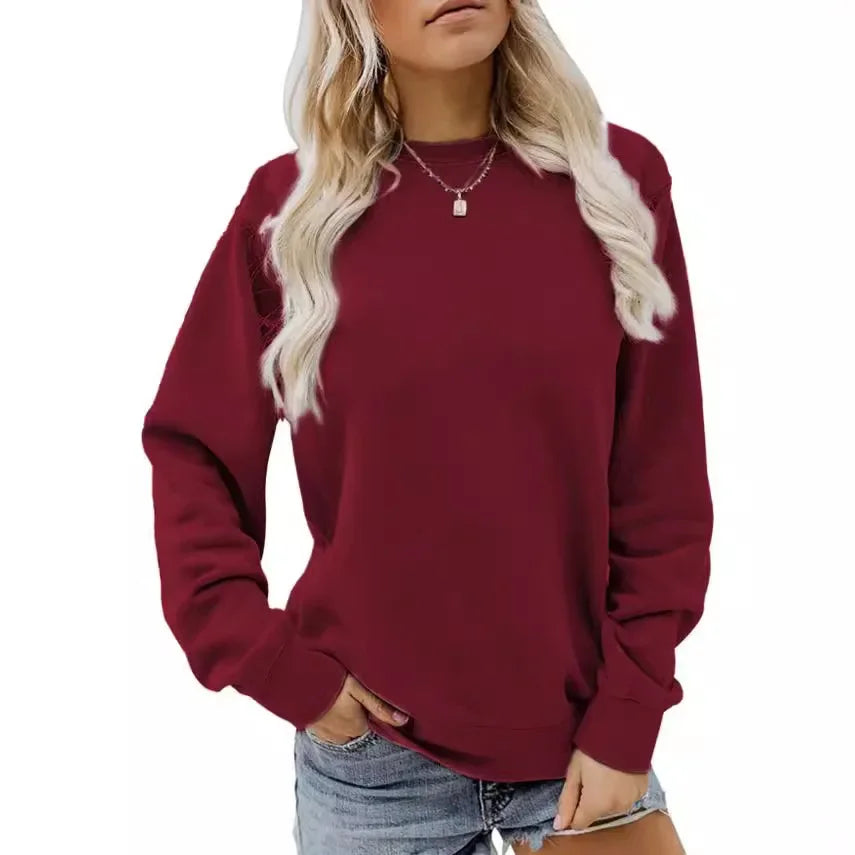 Femme portant un sweat-shirt rouge avec des manches longues et un col rond, associé à un short en jean. Elle porte également un collier délicat et adopte une pose décontractée.