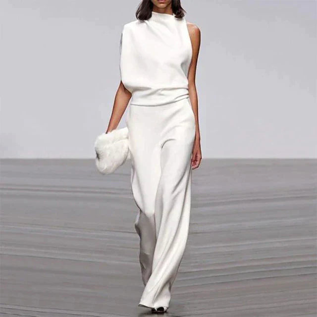 Abette | Combinaison chic pour femme en blanc, avec un haut asymétrique à une épaule et un pantalon fluide à jambes larges, parfait pour des occasions élégantes et des soirées, complété par un sac à main en fourrure blanche.