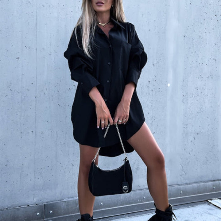 Chemisier oversize noir pour femme au style tendance, avec coupe ample, manches longues retroussées et fermeture boutonnée, porté comme une robe avec sac à main noir pour un look moderne et élégant.