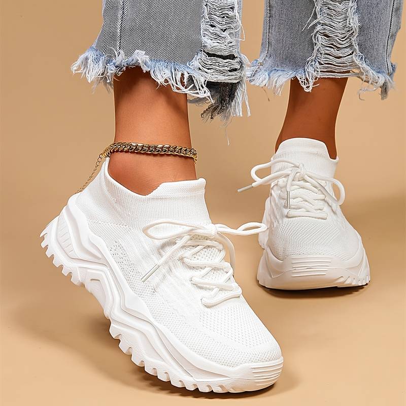 Modernes, baskets blanches en maille à lacets avec semelle épaisse crantée, vues de près et portées avec un jean effiloché sur fond beige.
