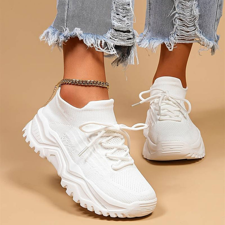 Modernes, baskets blanches en maille à lacets avec semelle épaisse crantée, vues de près et portées avec un jean effiloché sur fond beige.