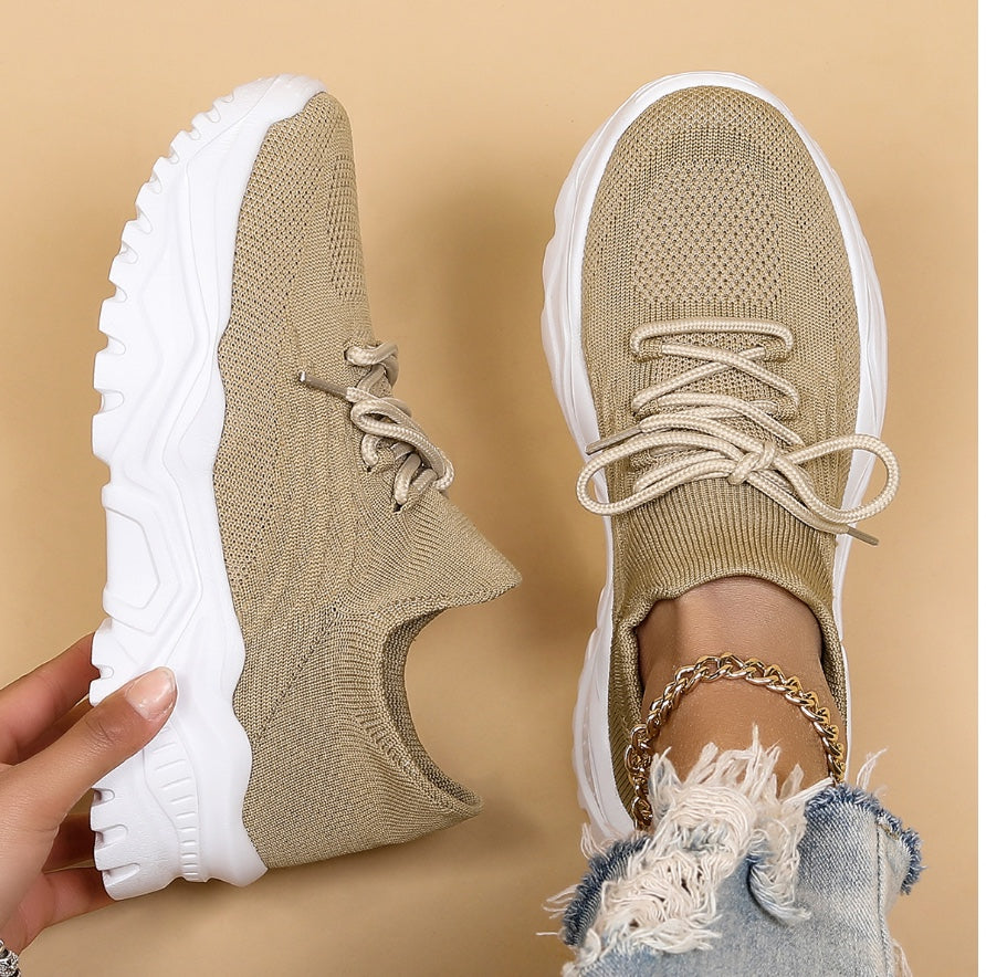Modernes, baskets kaki/beige en maille à lacets avec semelle blanche épaisse, une chaussure tenue à la main et l’autre portée, sur fond beige.