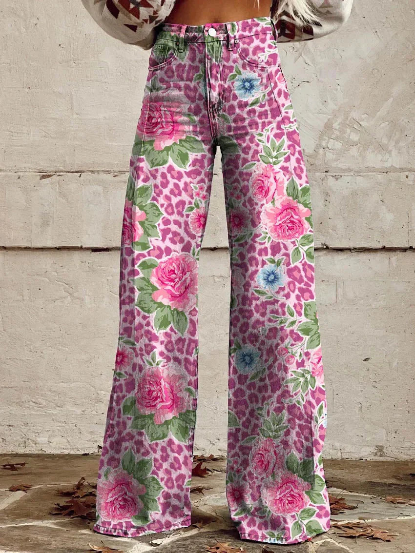 Jean ample pour femme Anouk taille haute, imprimé léopard rose avec grandes roses et petites fleurs bleues, coupe large et jambes évasées, porté devant un mur en béton.