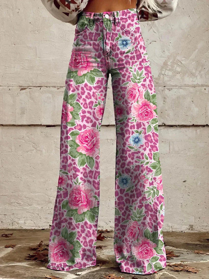 Jean ample pour femme Anouk taille haute, imprimé léopard rose avec grandes roses et petites fleurs bleues, coupe large et jambes évasées, porté devant un mur en béton.
