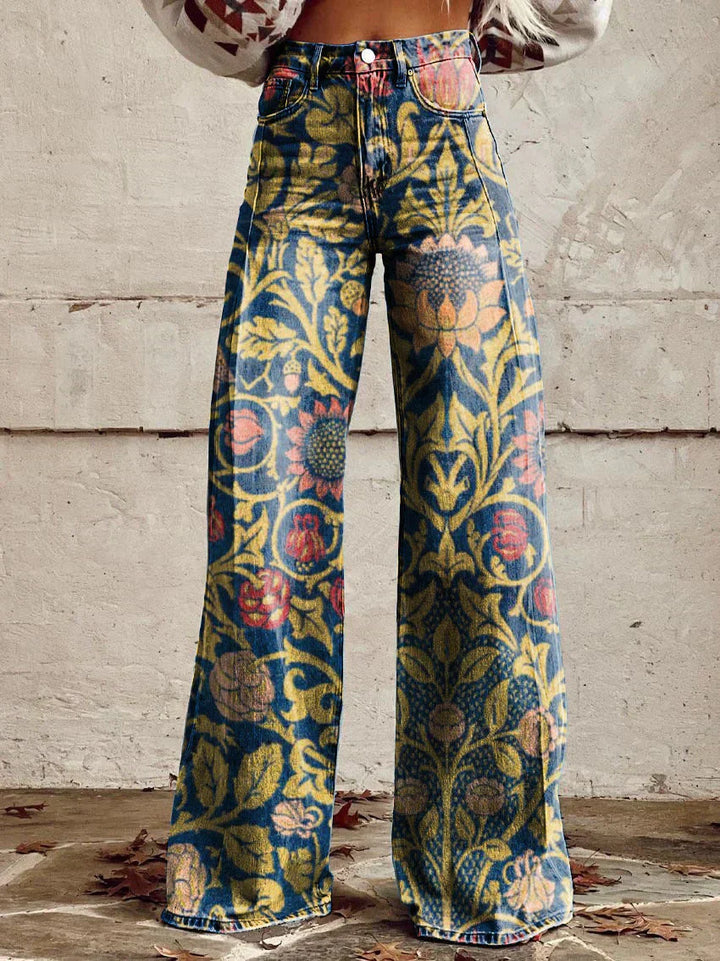 Jean ample pour femme Anouk taille haute, denim bleu à motif floral baroque doré avec touches rouges, coupe large et jambes évasées, porté devant un mur en béton.