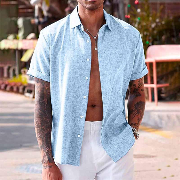 Chemise en lin moderne pour homme, modèle Antoine, de couleur bleu clair, à manches courtes, portée ouverte pour un style estival décontracté et élégant avec un pantalon blanc.