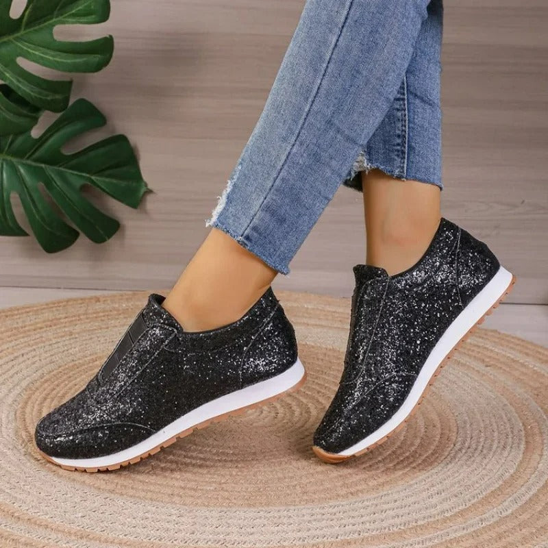 Baskets noires à paillettes, semelle blanche et gomme, portées avec un jean, posées sur un tapis rond.
