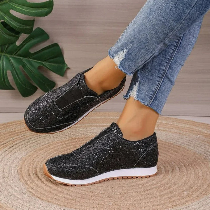 Baskets noires scintillantes avec empiècement élastique, semelle blanche et gomme, portées avec un jean, vue latérale.
