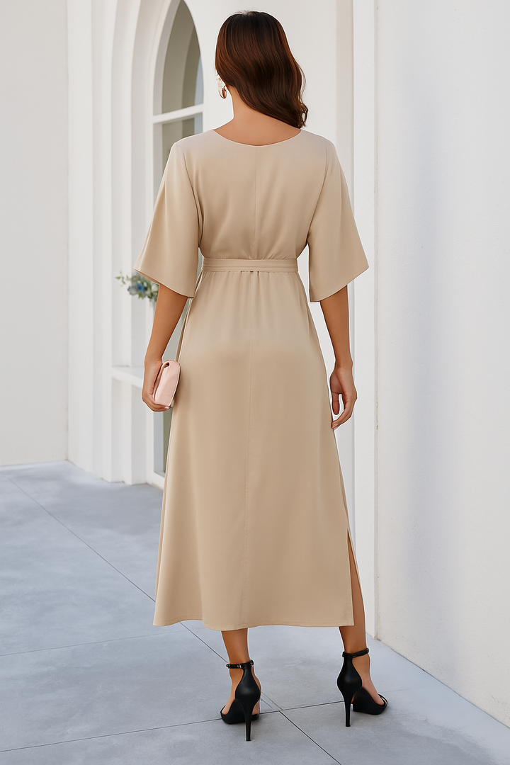 Vue arrière de la robe midi Audrey à col en V pour femme, avec une coupe fluide et élégante. Le lien à la taille met en valeur la silhouette, tandis que la fente latérale ajoute une touche moderne. Disponible en beige, cette robe tendance est parfaite pour les journées automnales et les occasions élégantes.