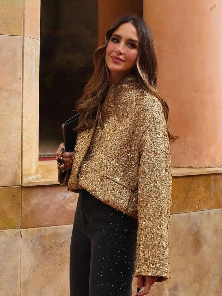 Femme élégante portant la veste bomber courte Aurélie en tissu doré scintillant, associée à un pantalon noir chic, un blouson tendance pour un look moderne et raffiné.