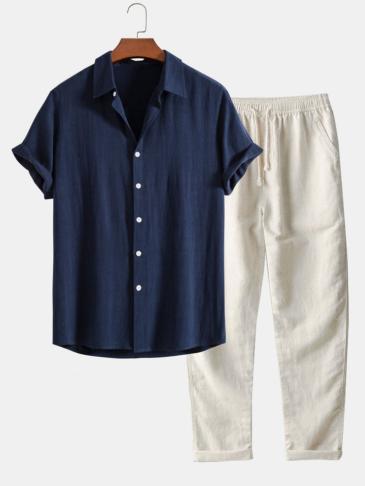 Ensemble élégant composé d'une chemise à manches courtes de couleur bleu marine avec des boutons blancs et d'un pantalon beige clair à taille élastique, offrant un look estival chic et confortable. Idéal pour les journées ensoleillées.