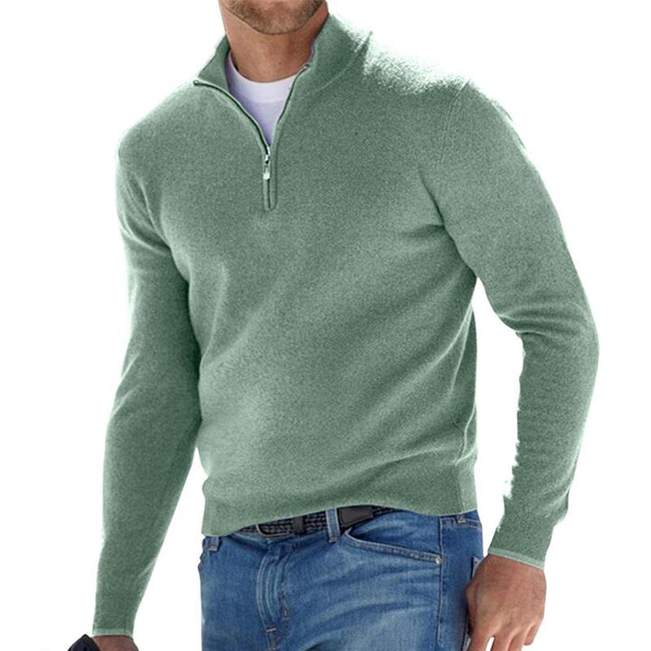 Homme portant le pull zippé pour hommes Basile en maille vert sauge, coupe moderne avec col montant et demi-zip, associé à un jean pour un look décontracté élégant.