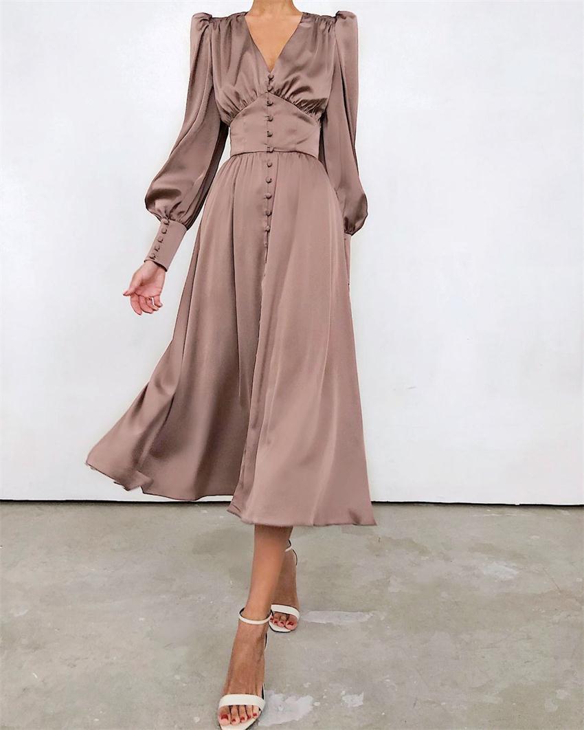 Robe en beige satiné, avec des manches longues bouffantes, un décolleté en V, des boutons sur le devant et une coupe fluide, idéale pour des occasions élégantes et des soirées formelles