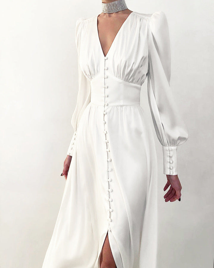 Robe en satin blanc, avec un décolleté en V, des manches longues bouffantes, une taille cintrée et des boutons sur le devant, offrant une allure élégante et sophistiquée pour des soirées ou des événements formels.