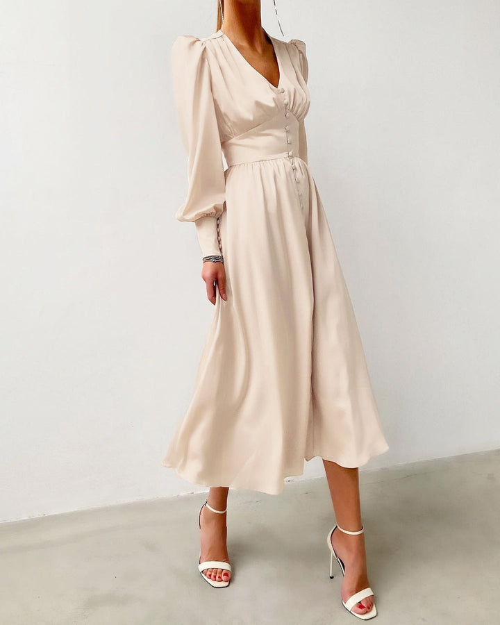 Robe en beige clair, avec un décolleté en V, des manches longues bouffantes et des boutons décoratifs, parfaite pour une soirée élégante ou un événement spécial.