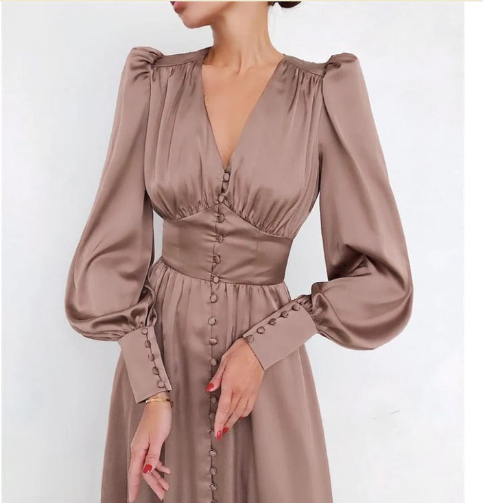 Robe en satin beige, avec des manches longues bouffantes, un décolleté en V, et des boutons décoratifs sur le devant, parfaite pour une soirée élégante ou un événement spécial."
