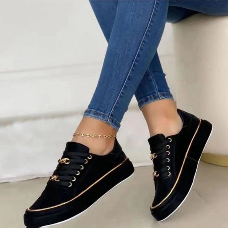 Baskets plateforme pour femme Blanche noires au style moderne, avec lacets et détails dorés, portées avec un jean bleu sur fond clair.