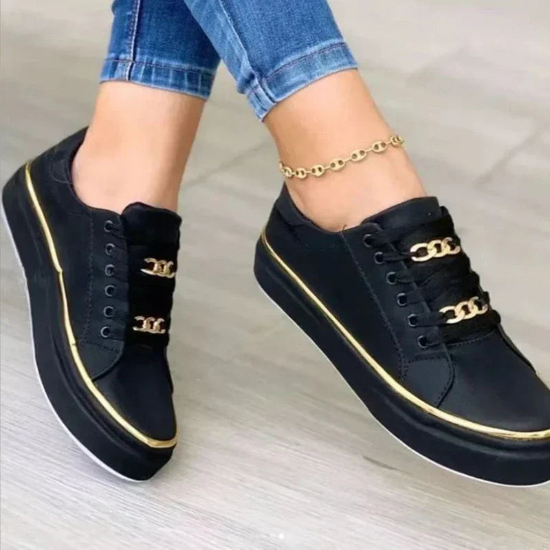 Gros plan des baskets plateforme pour femme Blanche noires, design moderne avec bordure dorée et lacets ornés de détails dorés, portées avec un jean.