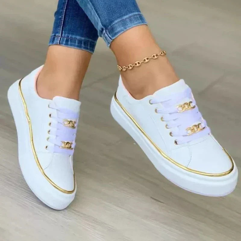 Gros plan des baskets plateforme pour femme Blanche blanches, design moderne avec bordure dorée et lacets ornés de détails dorés, portées avec un jean.