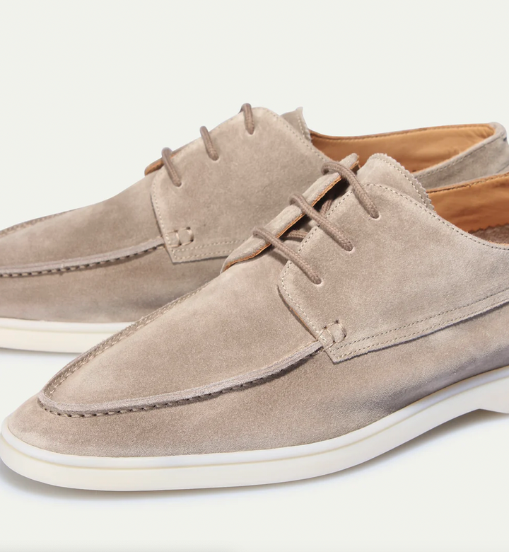 Gros plan sur les mocassins classiques pour hommes Boniface en daim beige, avec coutures apparentes, lacets et semelle claire, sur fond blanc.