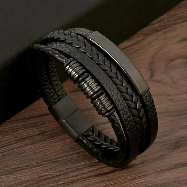 Bracelet homme Bruno moderne en cuir noir tressé multi-rangs, avec plaque métallique et anneaux décoratifs argentés, présenté sur fond bois.