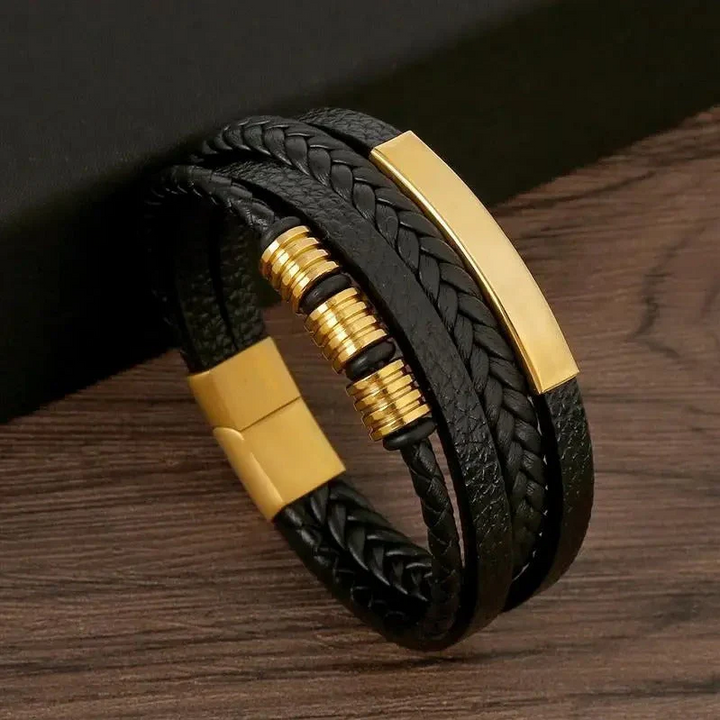 Bracelet homme Bruno moderne en cuir noir tressé multi-rangs, avec plaque métallique dorée, anneaux décoratifs et fermoir doré, posé sur fond bois.