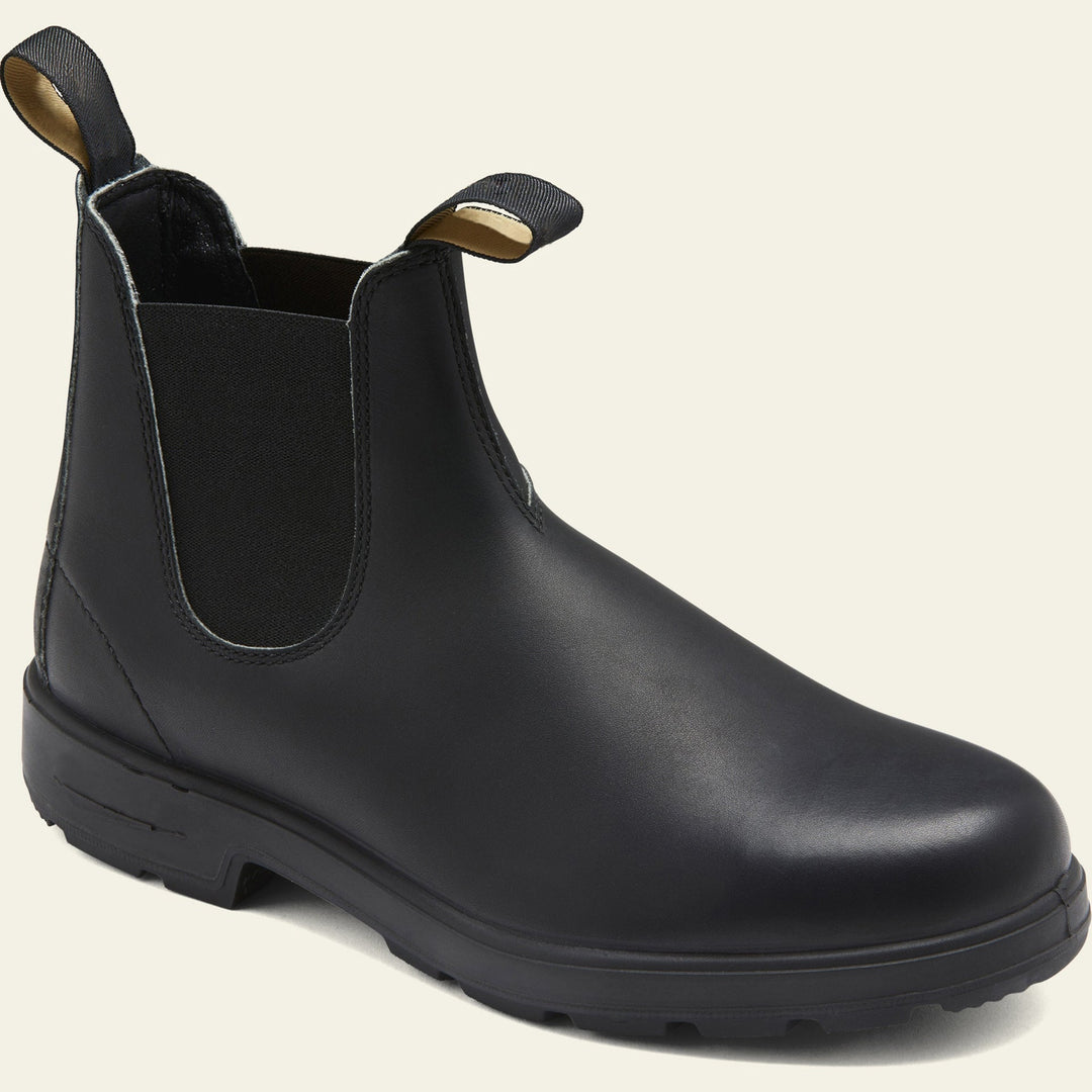 Vue latérale d’une paire de bottines en cuir noir mat pour femme, au design minimaliste et moderne. Les chaussures présentent des empiècements élastiques noirs sur les côtés pour un enfilage facile et deux languettes sur le devant et l’arrière pour plus de praticité. La semelle robuste en caoutchouc noir assure confort et stabilité, idéale pour un style chic et décontracté en toute saison.