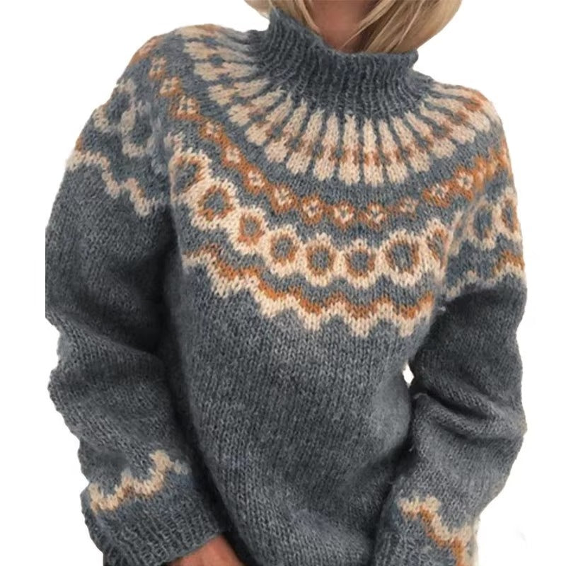 Femme portant un pull épais à col montant en maille moelleuse, dans des tons gris bleuté, beige et orange. Le pull présente un motif nordique géométrique sur le buste et les manches, offrant un style douillet, élégant et parfait pour la saison hivernale.