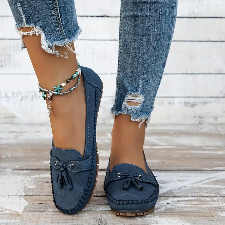 Des mocassins plats en suède bleu marine, dotés d'un nœud décoratif à l'avant et d'une semelle en caoutchouc pour un confort optimal. Ce modèle est parfait pour un look décontracté, chic et moderne, accompagné d'un jean déchiré et de bracelets bohèmes. Un choix idéal pour allier style et confort.