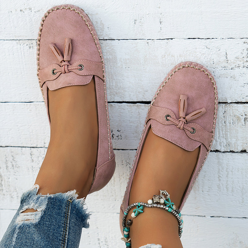 Vue de dessus des mocassins plats roses pour femmes, avec un nœud décoratif et une semelle intérieure confortable. Ce modèle au style moderne et décontracté est idéal pour un look élégant, accompagné d'un jean déchiré et de bracelets bohèmes. Parfait pour un confort au quotidien tout en restant stylée.