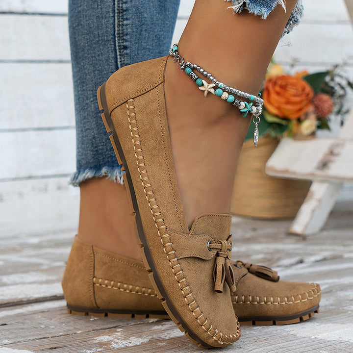 Des mocassins plats en suède beige avec un nœud décoratif, parfaitement associés à un jean déchiré et des bracelets bohèmes. Ce modèle allie confort et style moderne, idéal pour un look décontracté et tendance au quotidien.