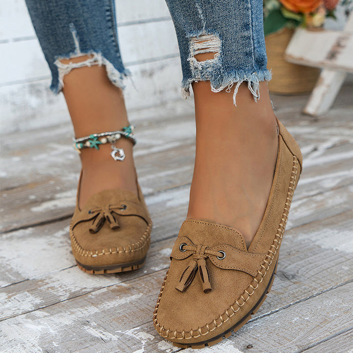 Des mocassins plats en suède beige, avec un nœud décoratif et une semelle en caoutchouc, parfaits pour un look décontracté et moderne. Ce modèle élégant est assorti à un jean déchiré et des bracelets bohèmes, créant une tenue à la fois stylée et confortable pour le quotidien.