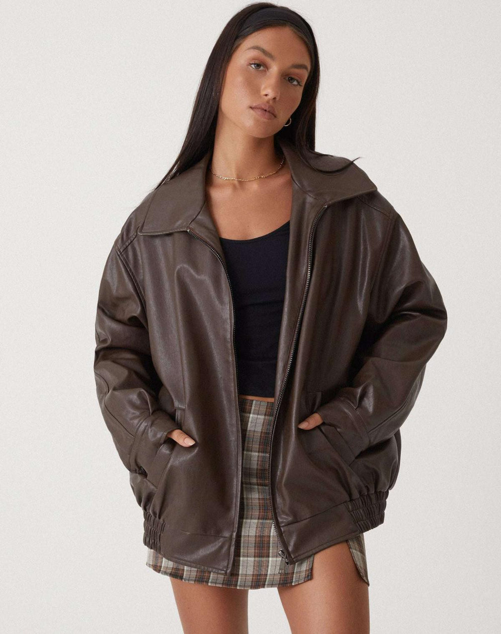 Veste oversize en PU pour femme, modèle Cécile. Veste en simili-cuir marron à la coupe ample, avec poches et taille élastiquée, portée avec une jupe à carreaux. Un look moderne et stylé pour l'hiver.