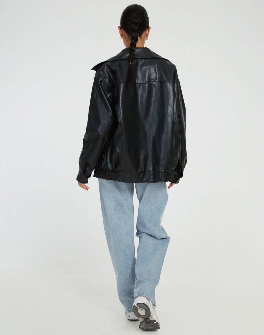 Vue arrière de la veste oversize en PU pour femme, modèle Cécile. Veste en simili-cuir noir avec coupe ample et taille élastiquée, portée avec un jean décontracté et des baskets. Un style moderne et confortable pour l'hiver.