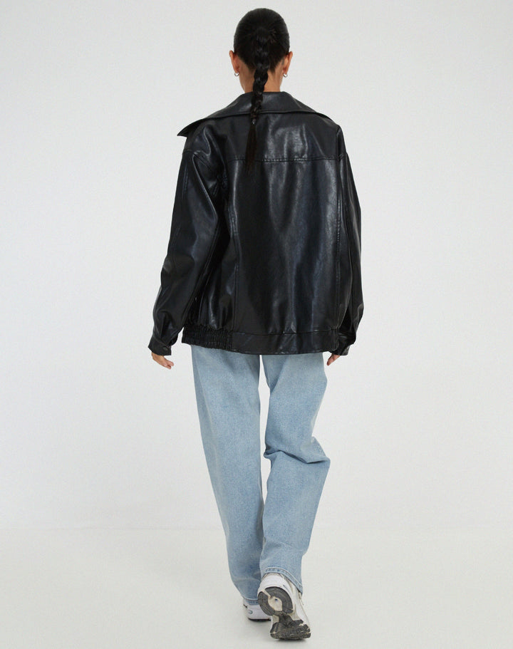 Vue arrière de la veste oversize en PU pour femme, modèle Cécile. Veste en simili-cuir noir avec coupe ample et taille élastiquée, portée avec un jean décontracté et des baskets. Un style moderne et confortable pour l'hiver.