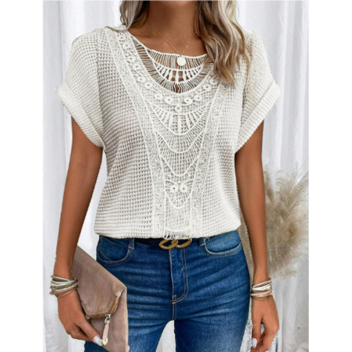 Haut d’été femme Cerise tendance, top blanc à manches courtes avec détail en dentelle ajourée au col, coupe fluide, porté avec jean bleu et pochette beige.
