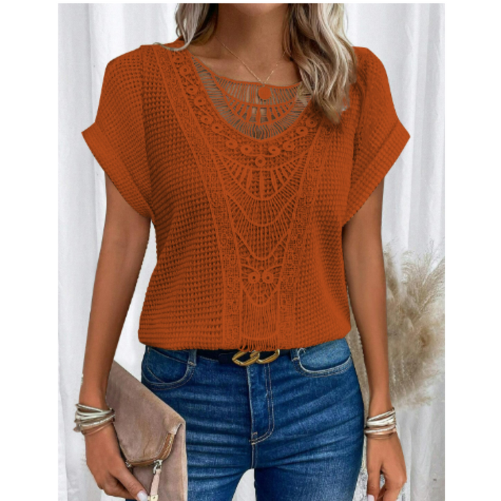 Haut d’été femme Cerise tendance, top orange à manches courtes avec détail en dentelle ajourée au col, coupe fluide, porté avec jean bleu et pochette beige.