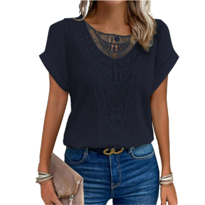 Haut d’été femme Cerise tendance, top bleu marine à manches courtes avec détail en dentelle ajourée au col, coupe fluide, porté avec jean bleu et pochette beige.