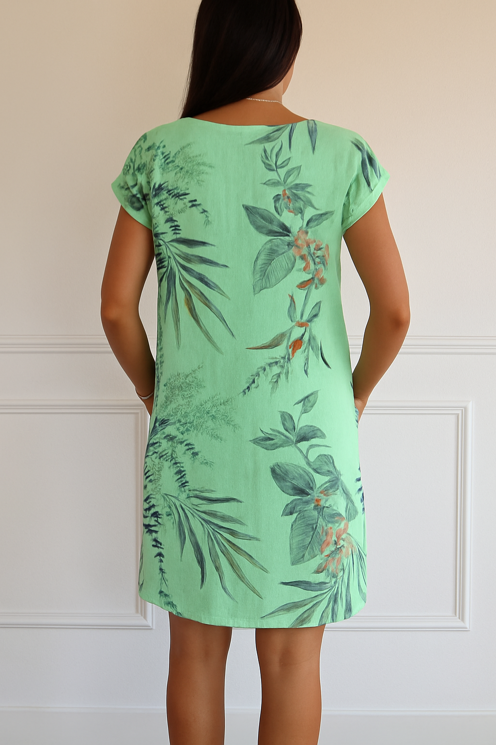 Vue arrière de cette robe d'été en lin vert pastel avec un imprimé tropical de feuilles et de fleurs. Cette robe décontractée offre un confort optimal avec ses poches latérales pratiques, idéale pour un look frais et estival.