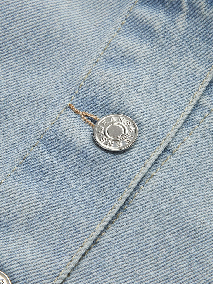 Zoom sur les boutons métalliques de la veste en jean courte Clementine, avec un design épuré et moderne. Ces boutons argentés ajoutent une touche de finition élégante à la veste, complétée par le tissu en denim bleu clair. Ce détail subtil souligne le style tendance et décontracté de cette pièce incontournable.